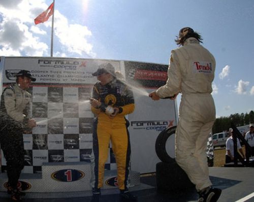 Simona De Silvestro, Jonathan Summerton, Frederic Vervisch spuiten met champagne op het podium in New Jersey