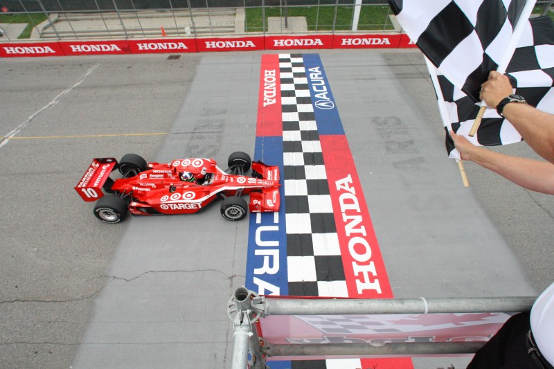 Dario Franchitti komt als eerste onder het zwart/wit geblokt door